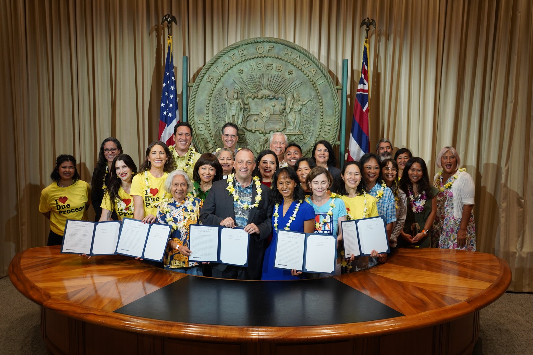 Governor Josh Green, legislators, and Campaign for Immigrant Justice advocates holding the signed bills at the Hawaiʻi State Capitol