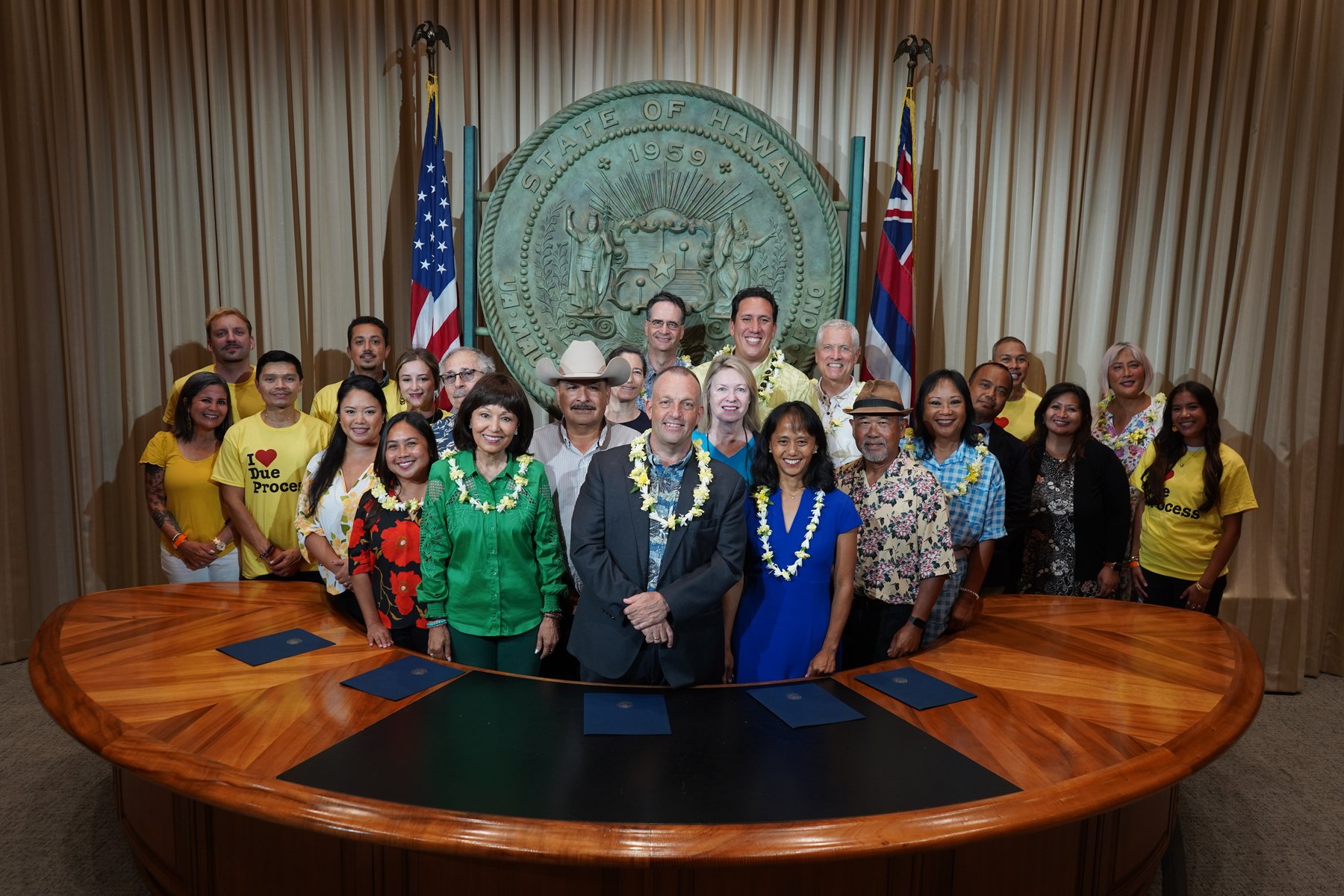 Coalition members, advocates, and Governor Josh Green with lei at the bill signing ceremony in front of the State of Hawaiʻi seal